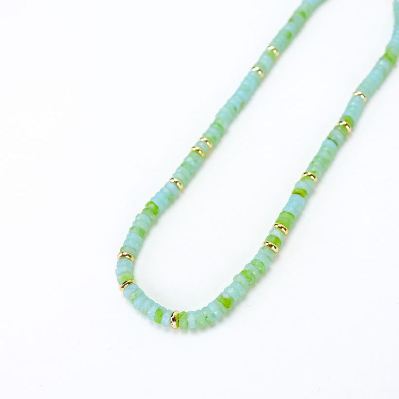 Necklace with light blue and green beads and gold accents on a white background