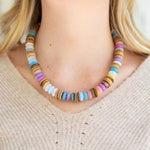 Colorful pink, white, blue and coconut wood beaded necklace worn by a person with a neutral background