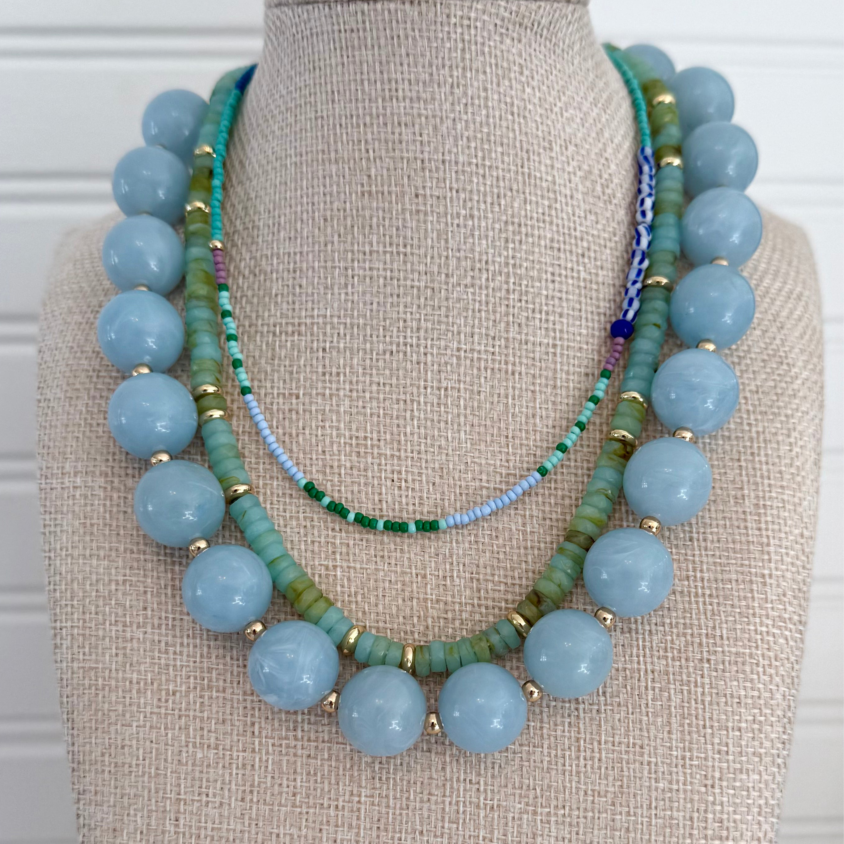 Necklace with blue chunky beads and green beads on a mannequin bust.