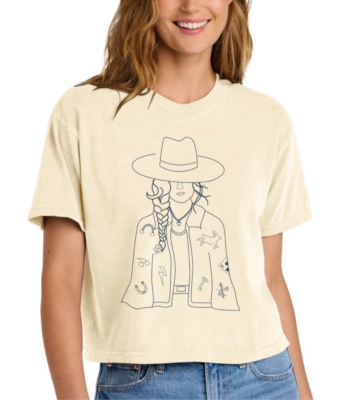 Person wearing a cream t-shirt with a graphic design of a person in a hat and jacket.