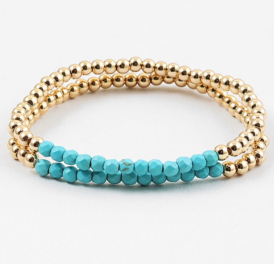 Stack of gold and turquoise beaded bracelets on a white background