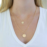 Gold necklace stack with disc pendants on a person wearing a white top