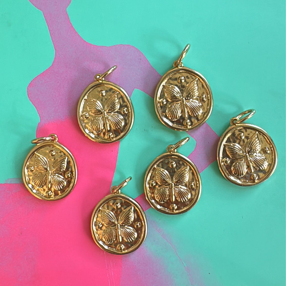 Gold butterfly disc pendants on a colorful abstract background