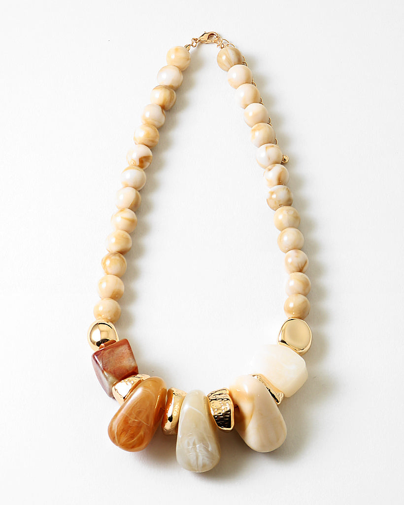 Necklace with beige beads and large decorative stone and gold elements on a white background
