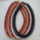 Multicolored beaded necklaces in red, orange, beige, white and blues on a textured white background