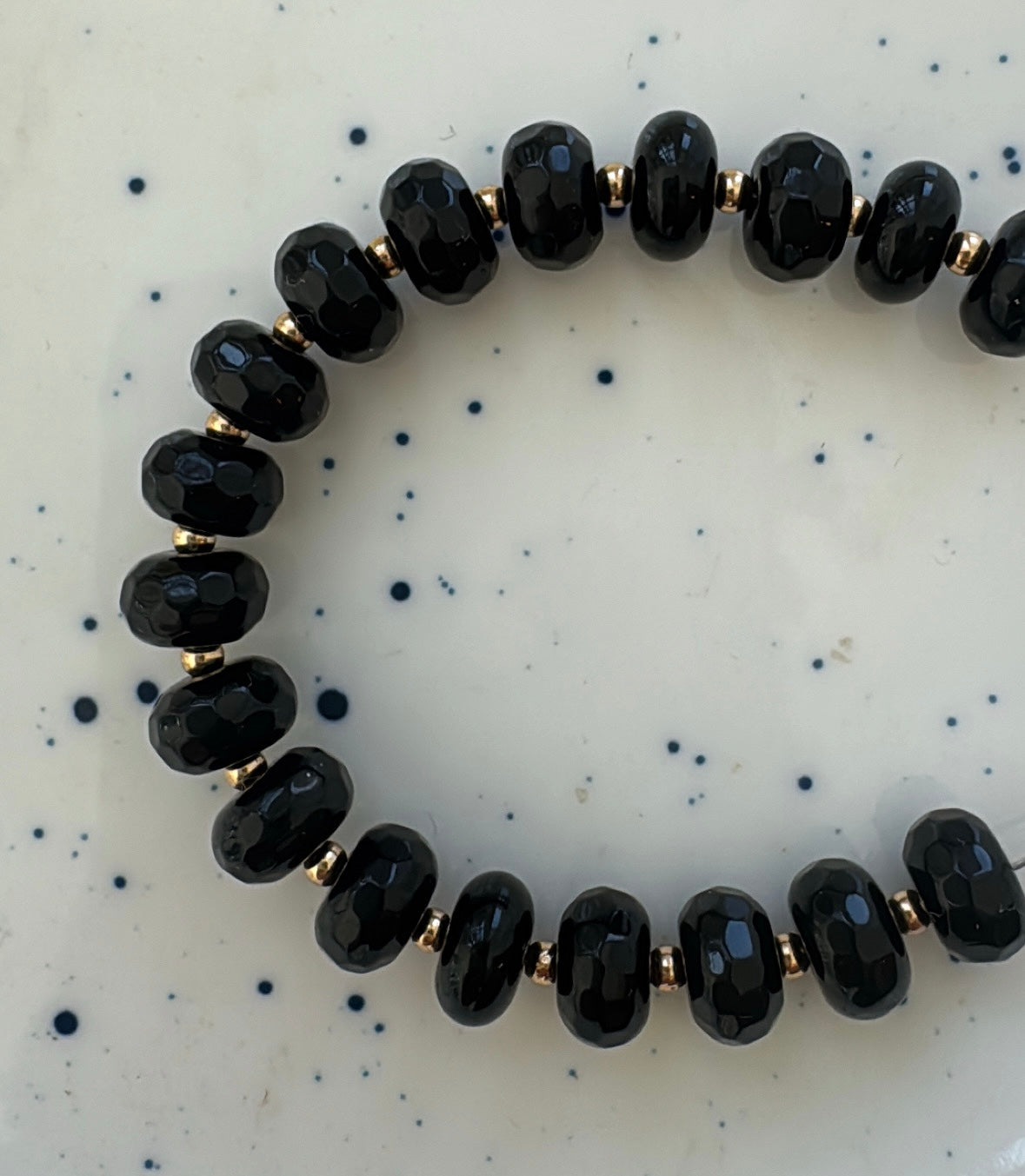 Black beaded strand of beads on a speckled white background