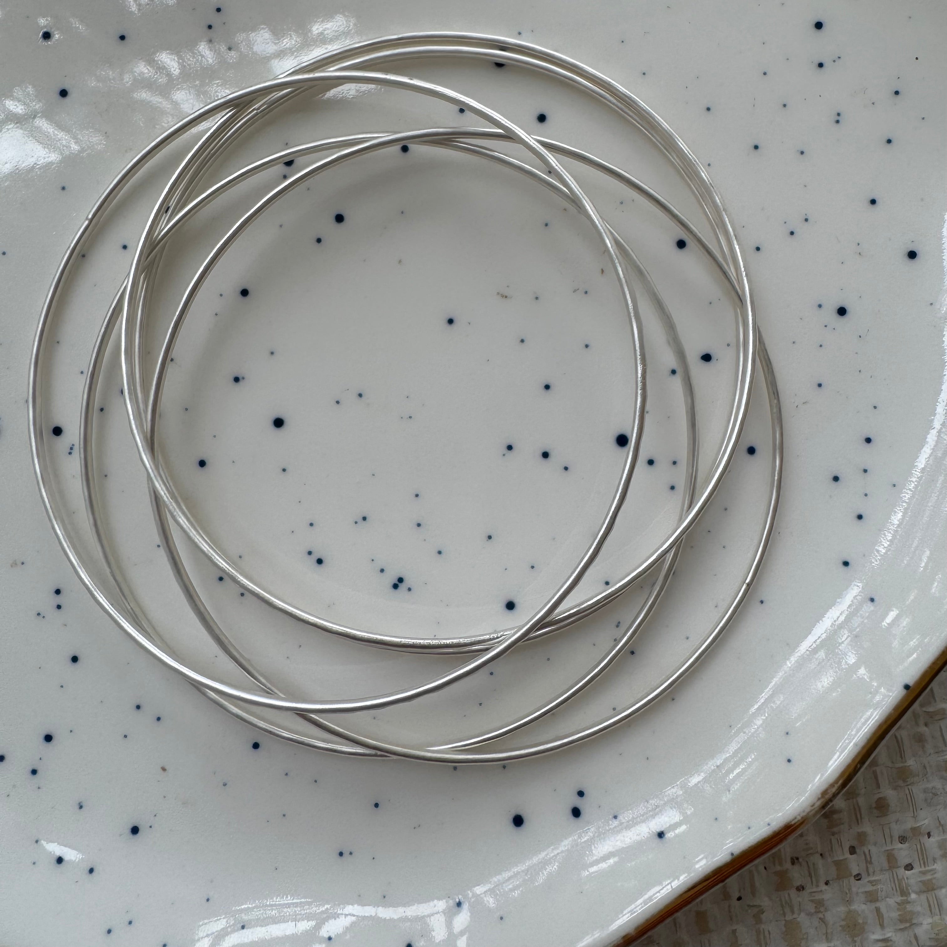 Stack of silver bracelets with a speckled pattern on a matching speckled surface.