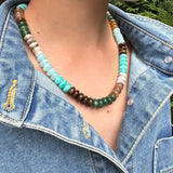 Necklace with multicolored blue, brown and tan beads worn by a person in a denim jacket.