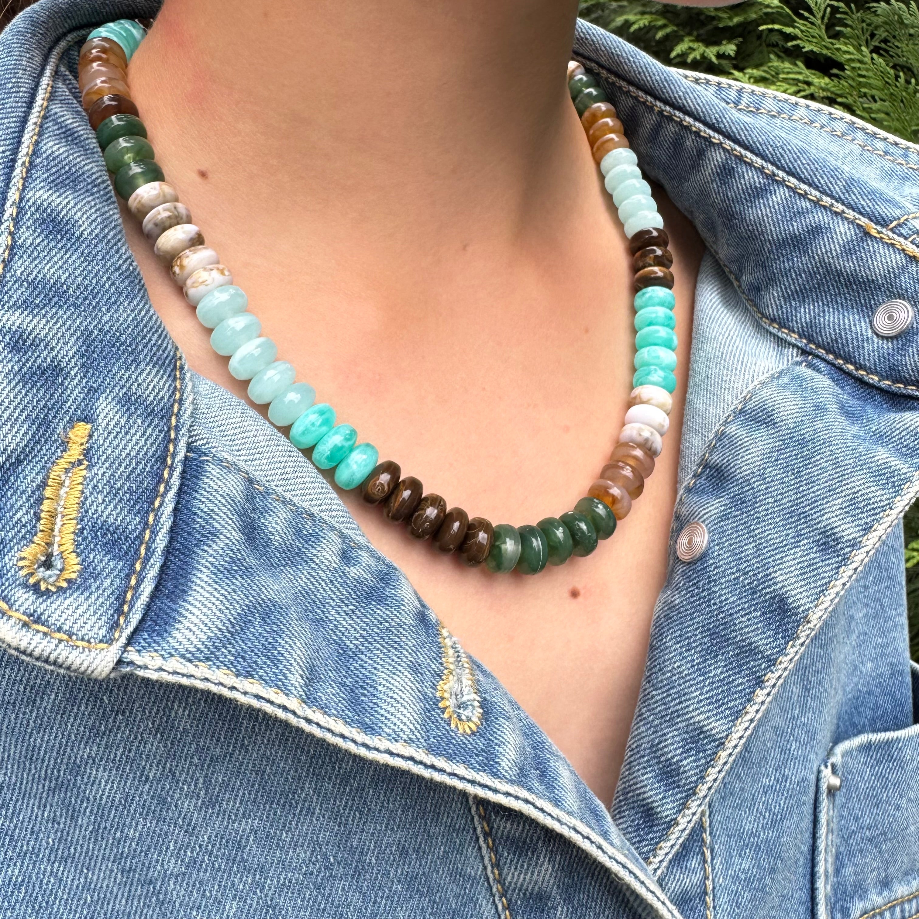 Necklace with multicolored blue, brown and tan beads worn by a person in a denim jacket.