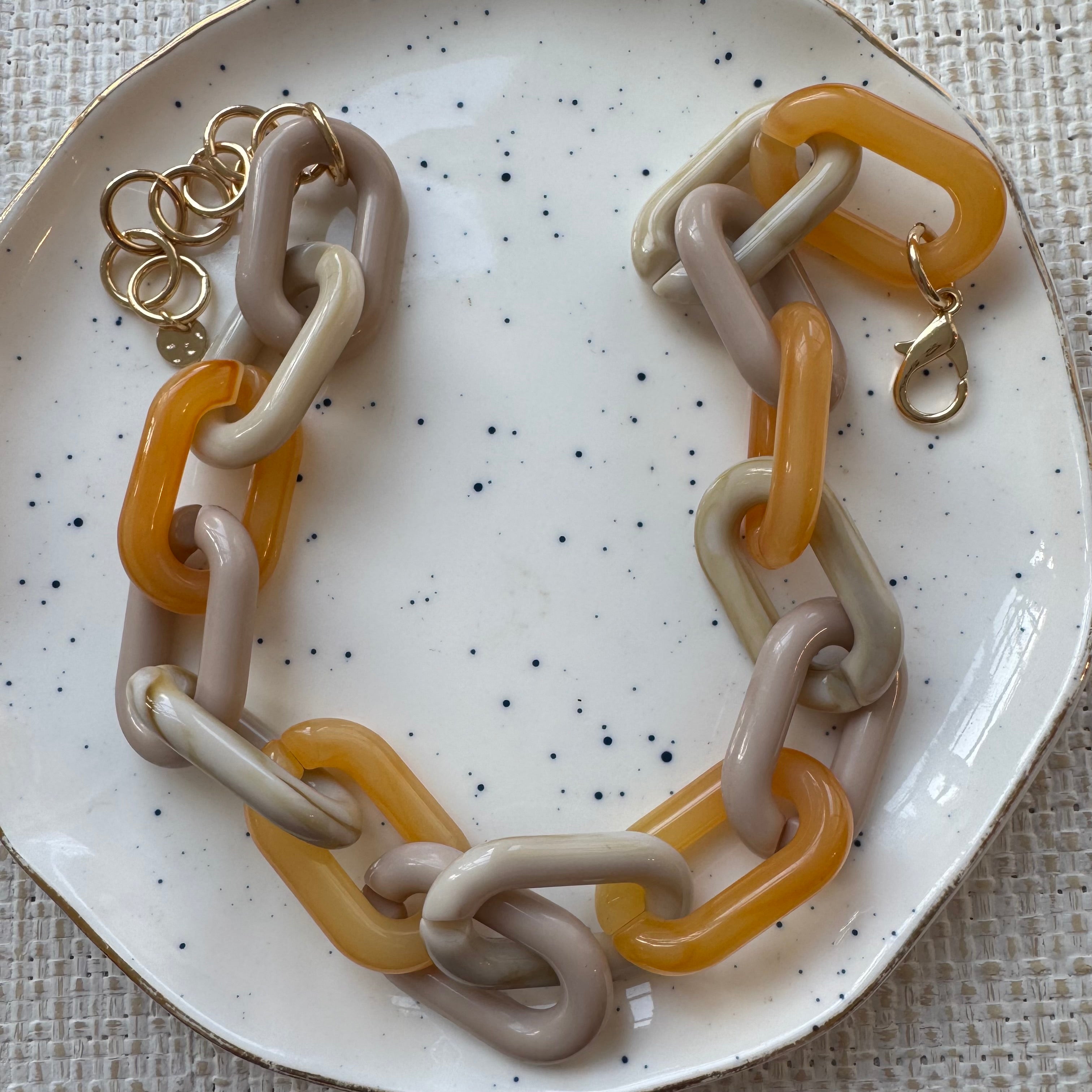 Necklace with chain links made of cream and orange on a speckled plate