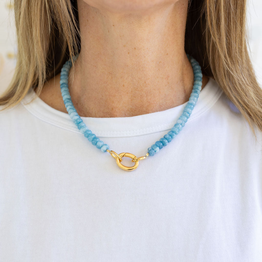 Blue beaded necklace with a gold clasp worn by a person on a white background