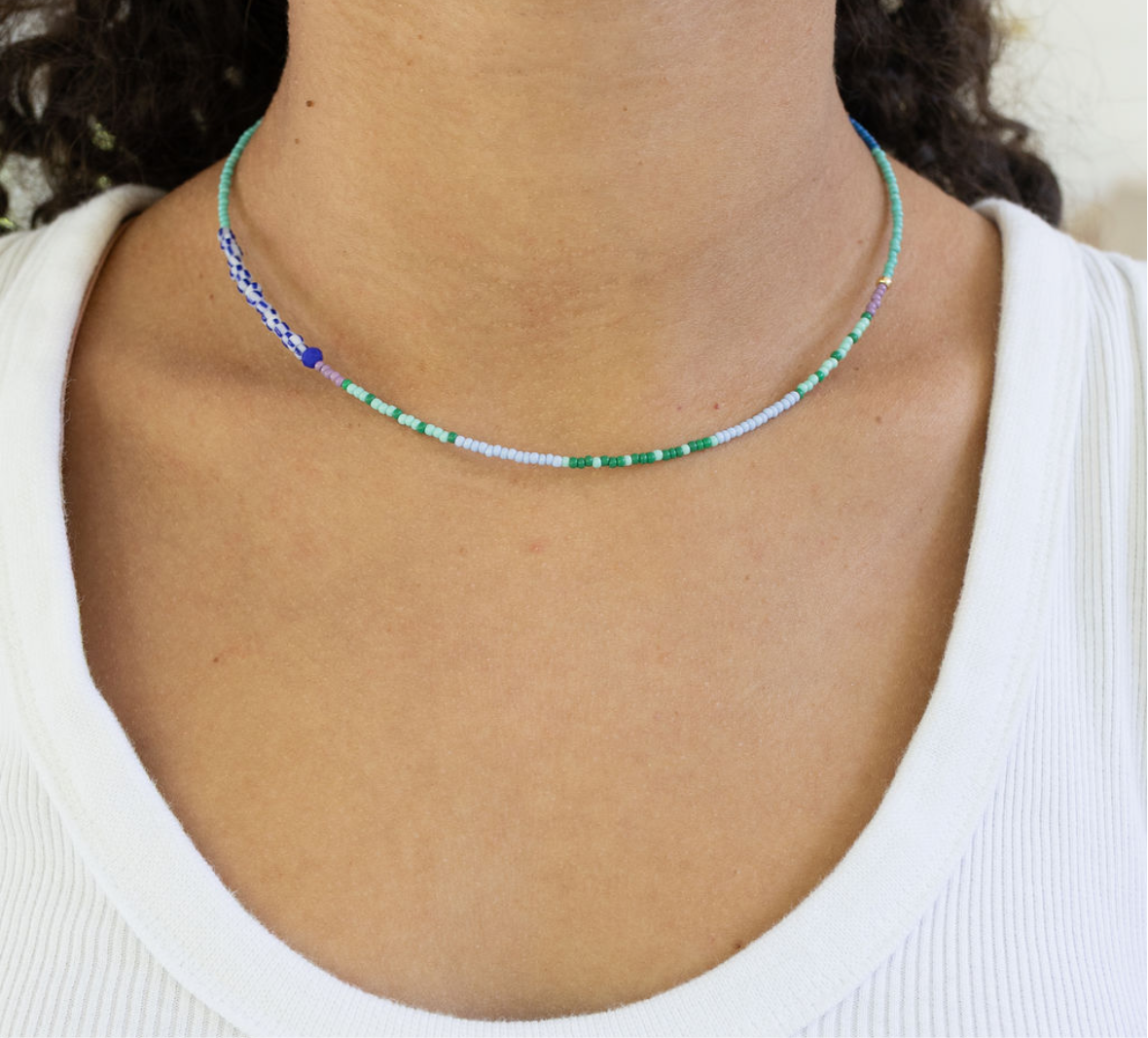 Dainty bead necklace in blues and greens on a woman's neck.