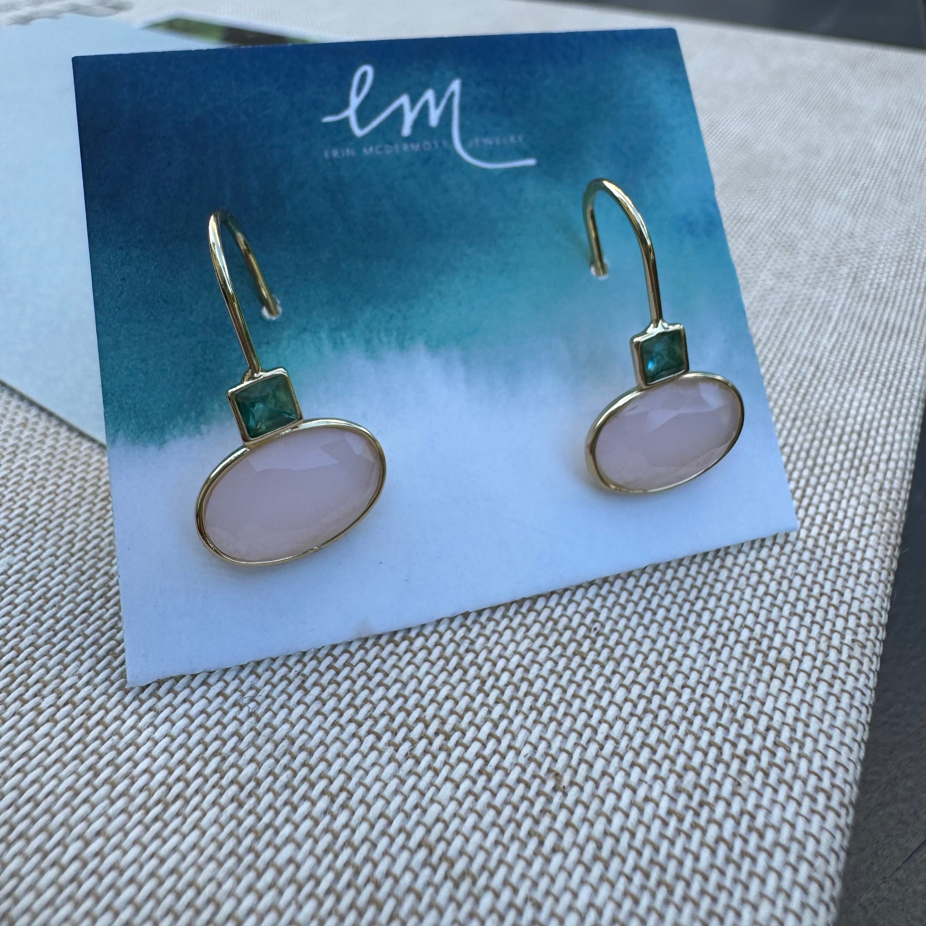 Pair of pink and green stone dangle earrings on a branded card with a textured surface background