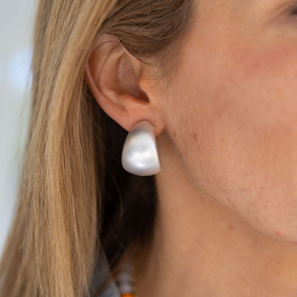 A close-up image of a person wearing a thick silver hoop earring.