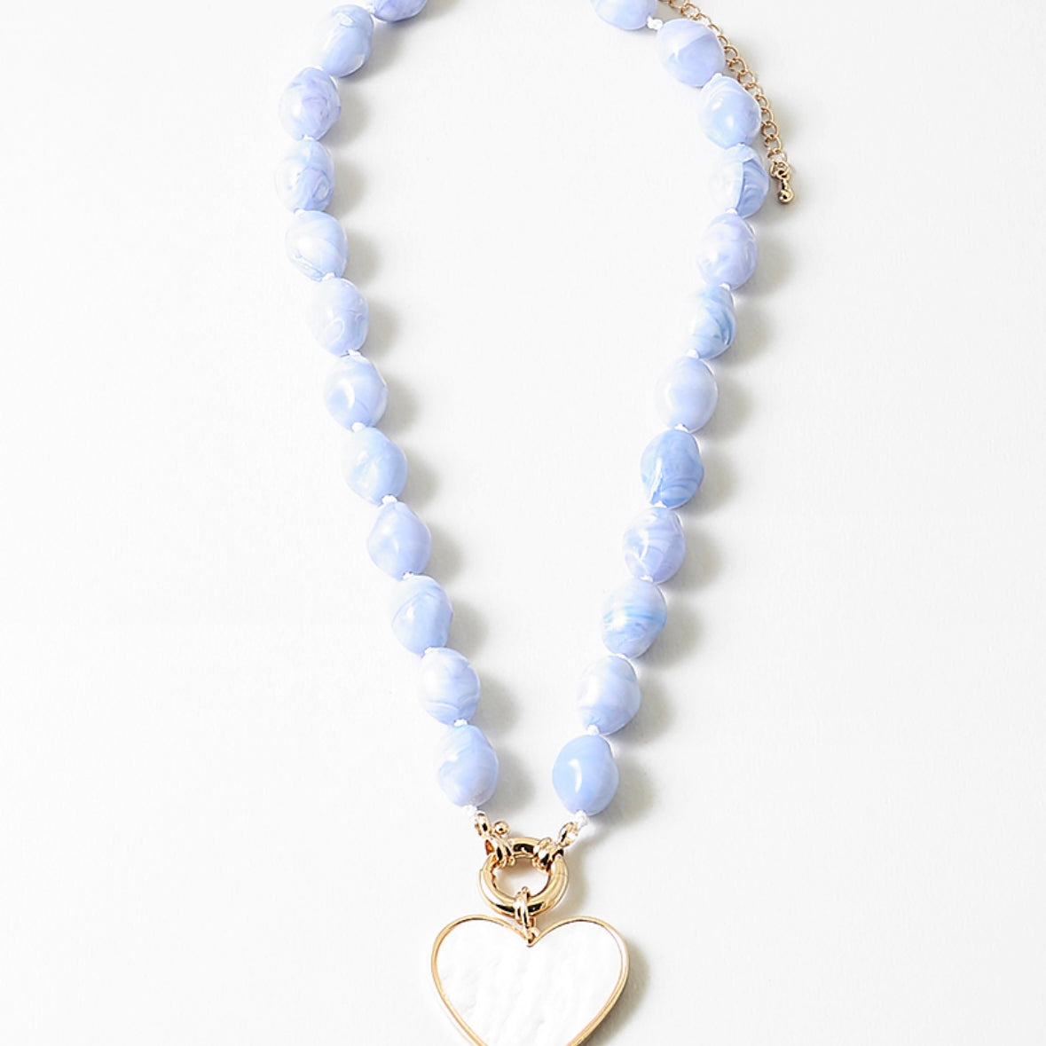 Necklace with light blue beads and a gold and white enamel heart pendant on a white background