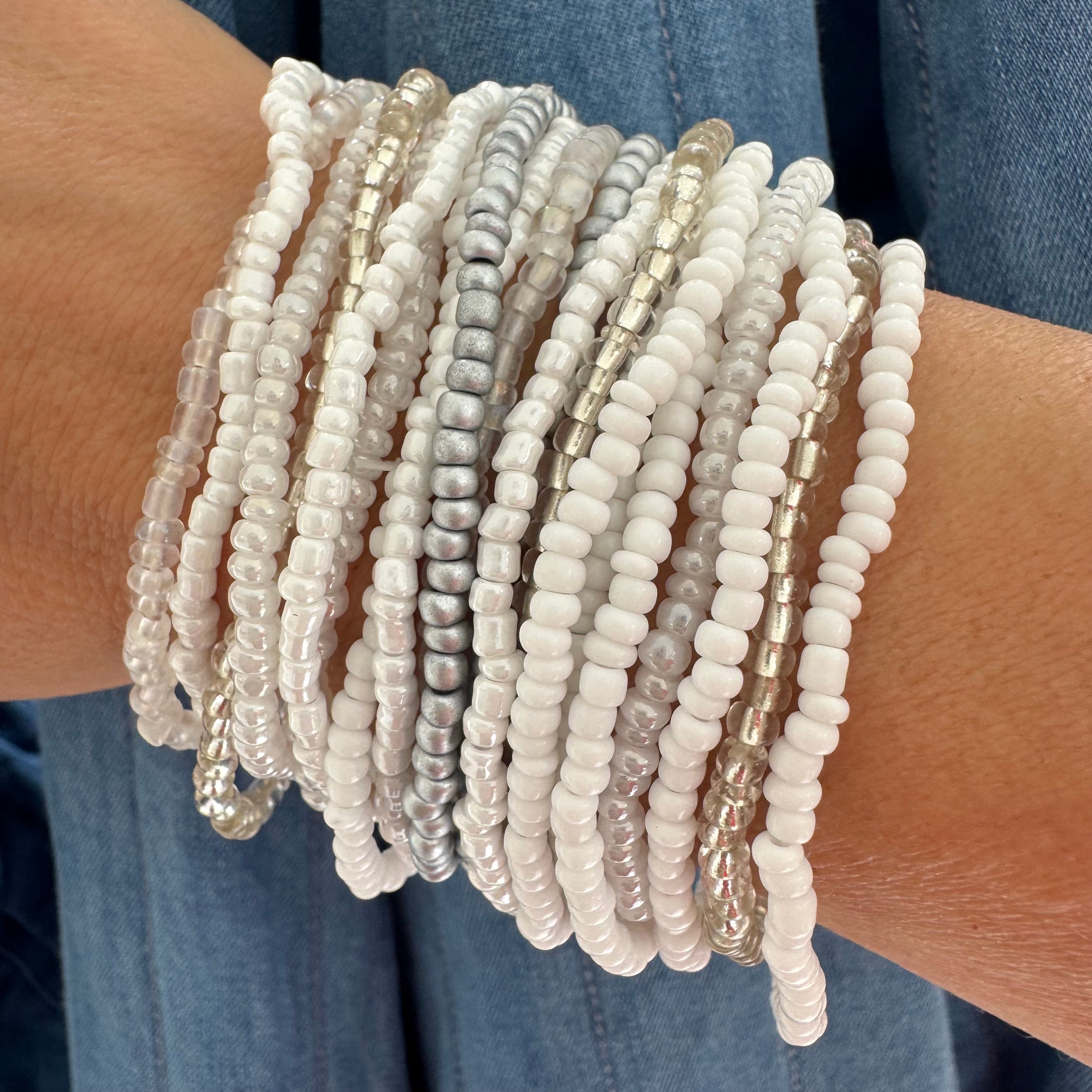 Multiple white and pearlescent beaded bracelets on a wrist with a denim background