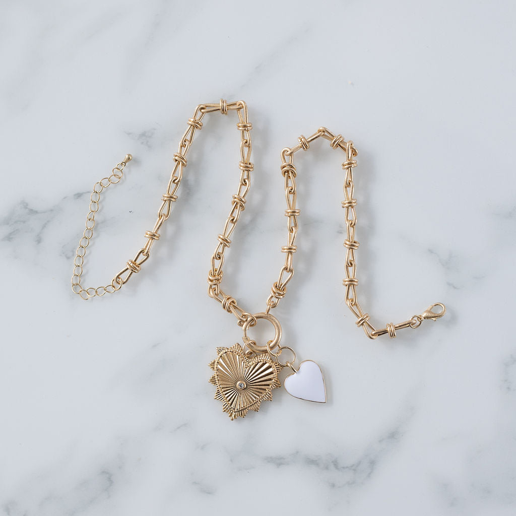 Picture of gold toggle chain with a large gold heart pendant with a diamond at its center and a white heart charm.