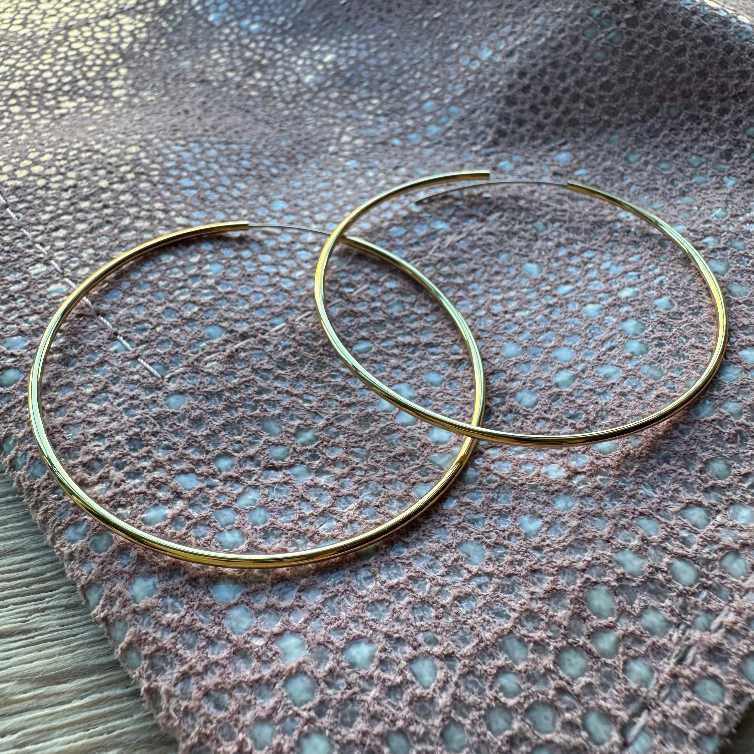 Two gold hoop earrings on a textured fabric surface