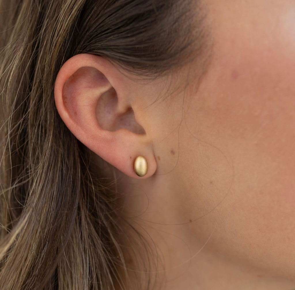 Model wearing a small brushed gold oval stud.