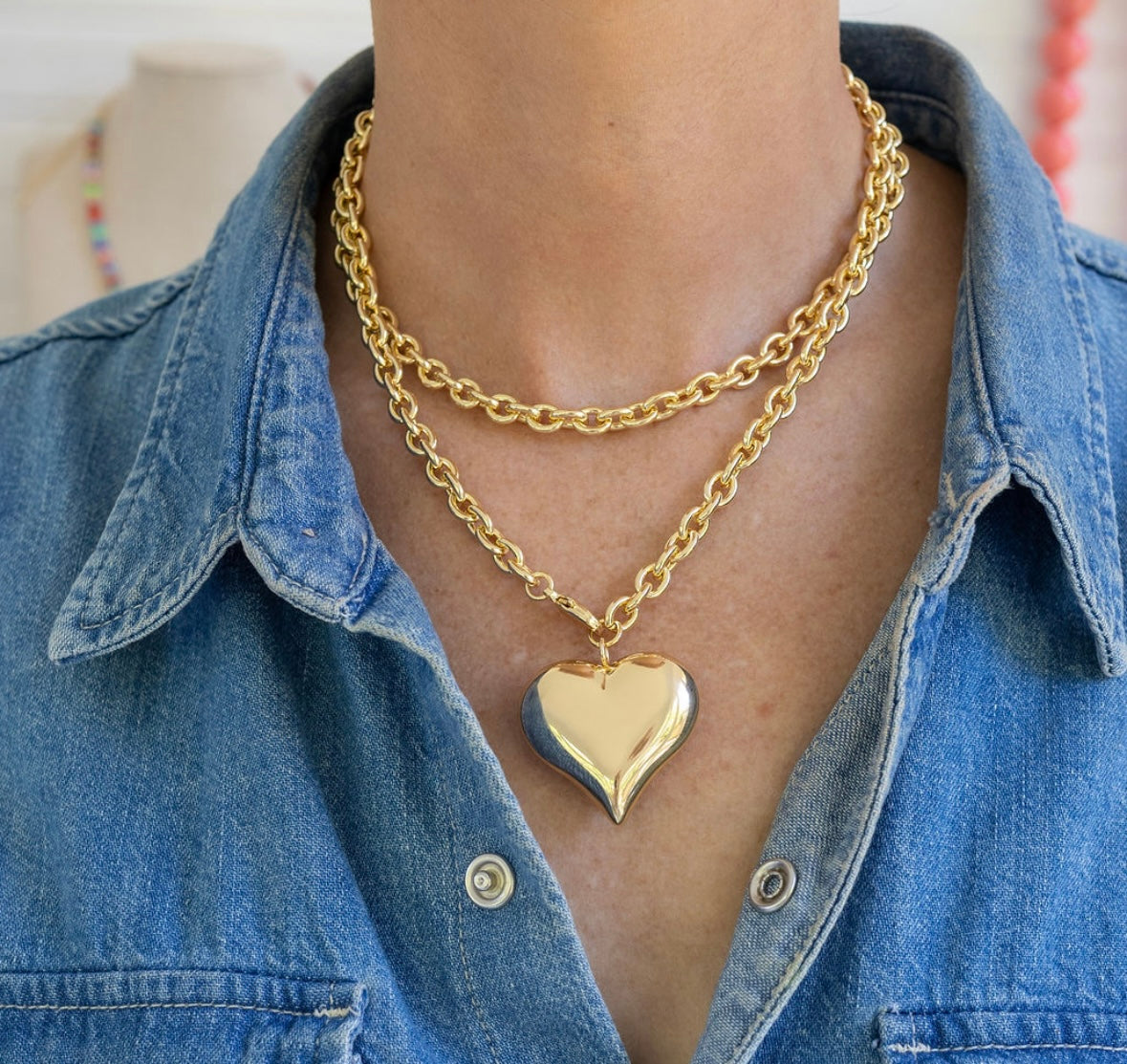 Gold chain necklace with a puffy heart pendant worn by a person in a denim shirt.