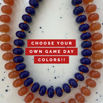 Necklaces with blue and orange beads on a white background with text 'Choose Your Own Game Day Colors!!'.
