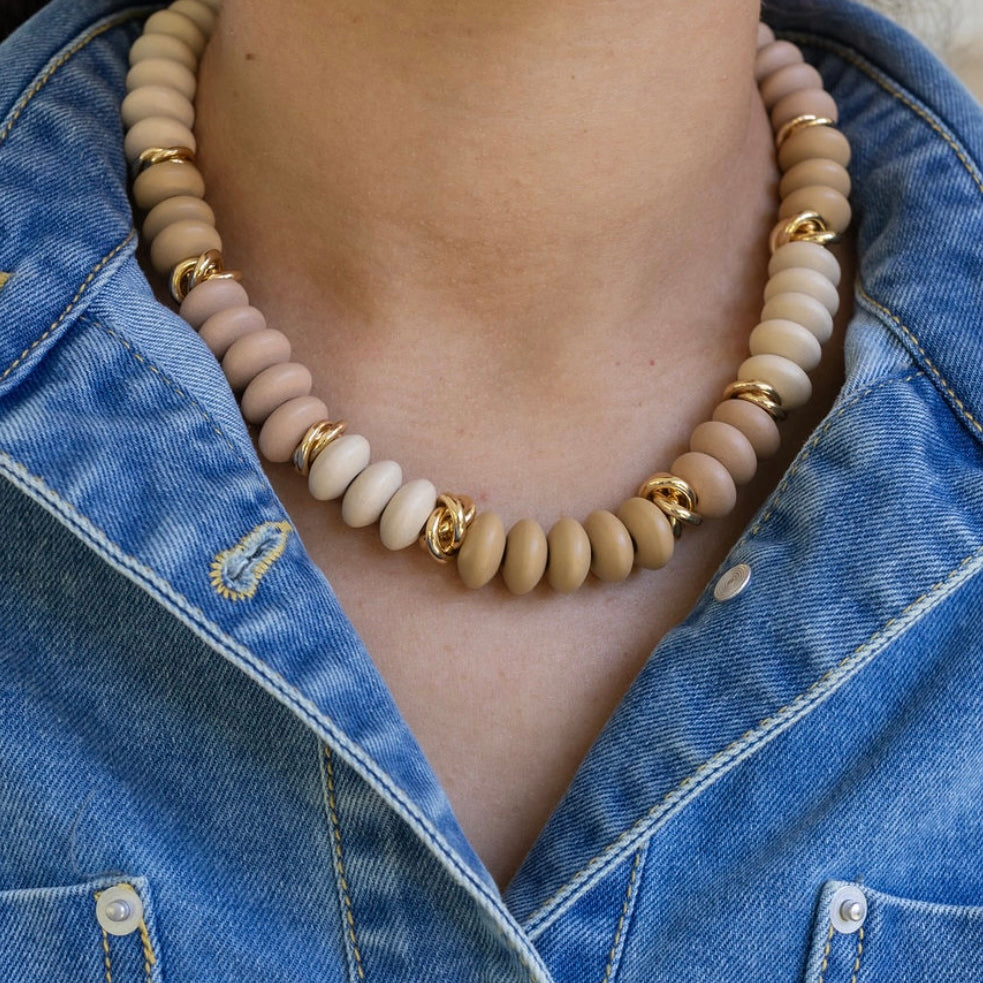 Necklace with beige beads and gold accents worn by a person in a denim jacket.