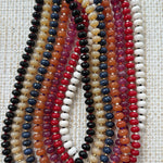 Set of multicolored beaded necklaces in blues, tans, oranges, reds and whites on a textured fabric background