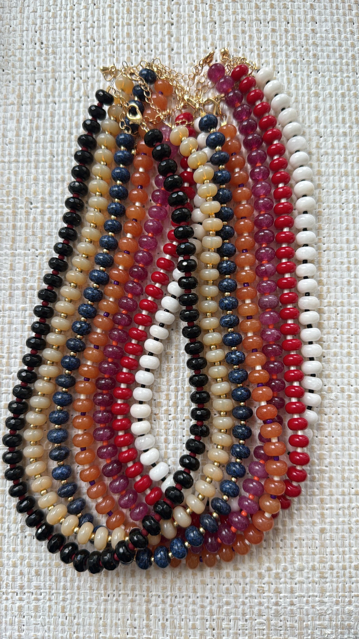 Set of multicolored beaded necklaces in blues, tans, oranges, reds and whites on a textured fabric background