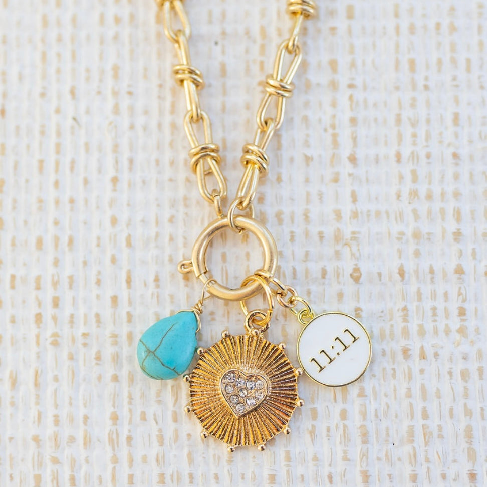 Picture of gold toggle chain with various charms attached.  One is a turquoise tear drop charm, gold textured disc with diamond heart in the center and white 11:11 disc.