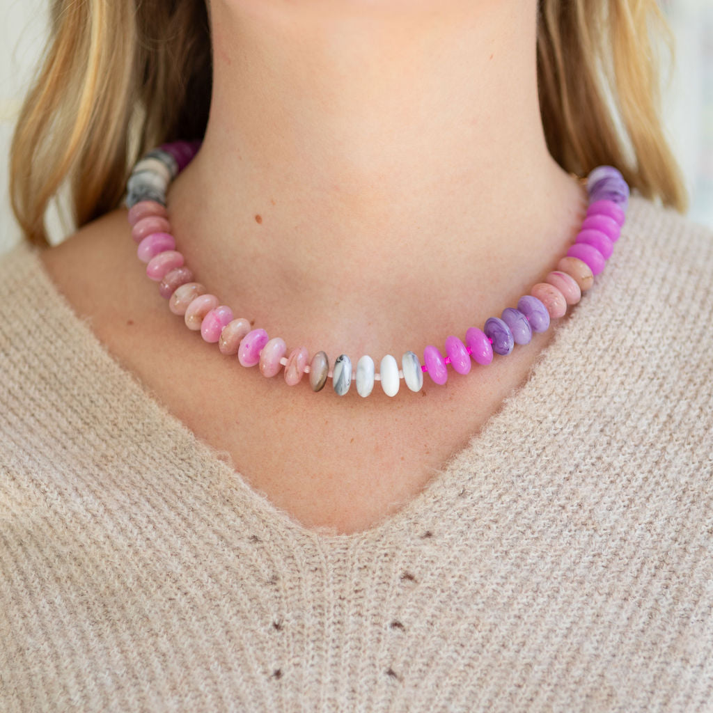 Necklace with multicolored pink and purple beads worn by a person in a beige sweater.