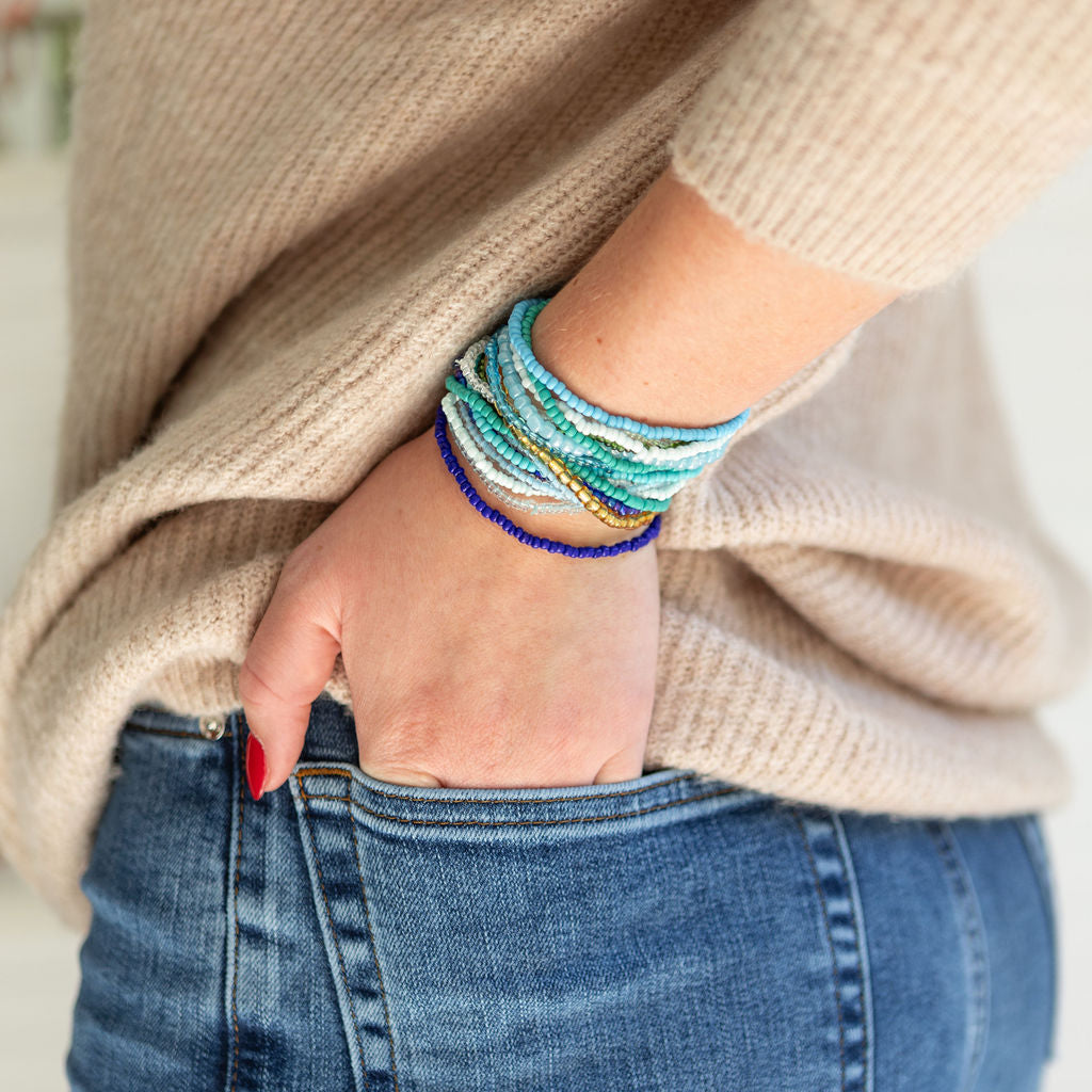 Person wearing multiple blue colorful bracelets on a neutral background