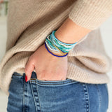 Person wearing multiple blue colorful bracelets on a neutral background