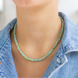 Person wearing a green beaded necklace with a denim jacket