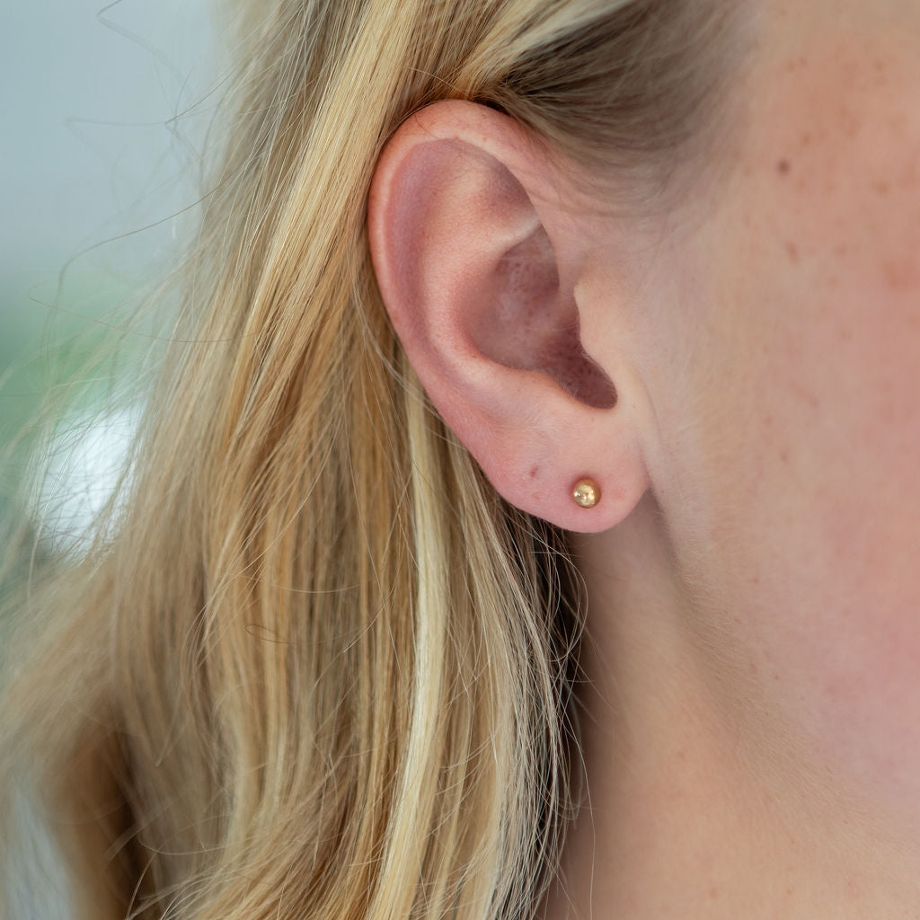 Close-up of an ear wearing a gold stud earring with blurred background