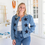 Woman wearing a denim jacket with star patterns in a bright room.