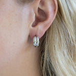Close-up of an ear wearing silver hoop earrings with blonde hair.