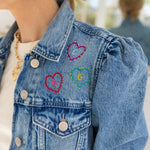 Close-up of a custom denim jacket with colorful embroidered hearts on the upper left side.