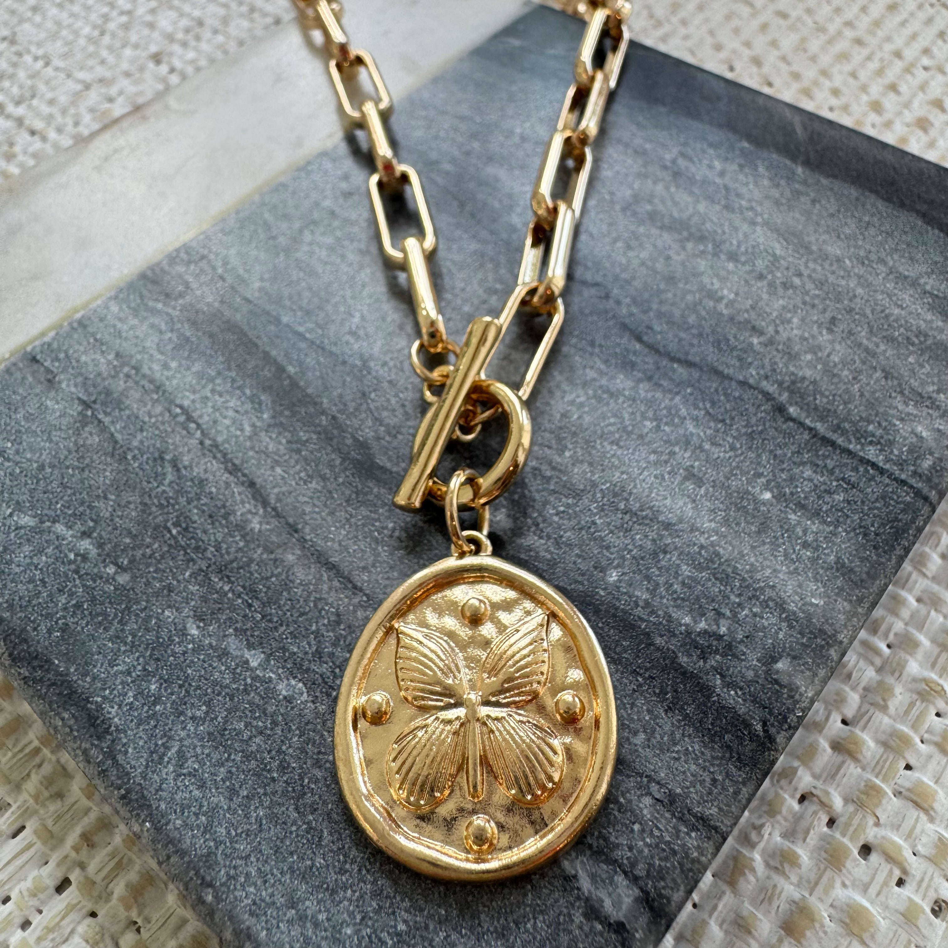 Gold necklace with a butterfly pendant on a stone surface