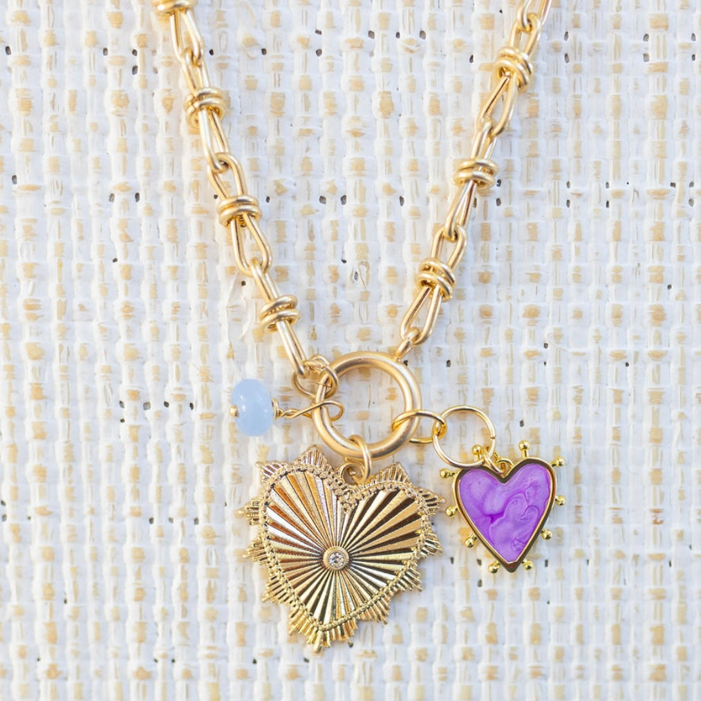 Picture of gold toggle chain that has a blue bead charm, purple heart charm and large gold heart pendant with diamond at the center.