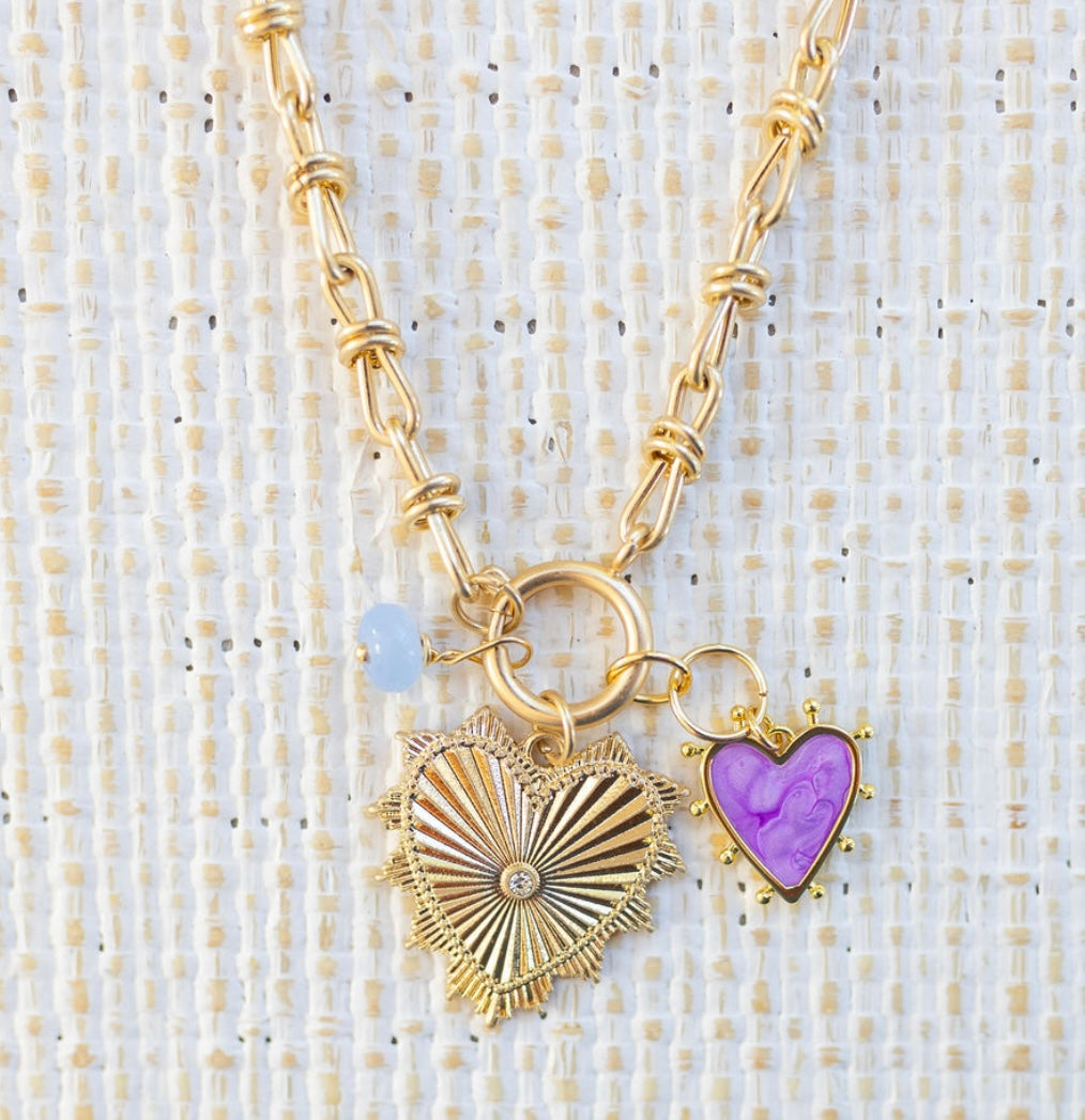 Picture of gold toggle chain that has a blue bead charm, purple heart charm and large gold heart pendant with diamond at the center.