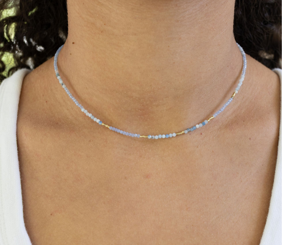 Picture of a woman wearing a delicate bead necklace in tiny white, gold and blue beads.