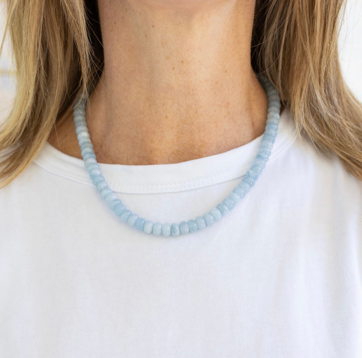 Light blue beaded necklace worn by a person with blonde hair, against a white background