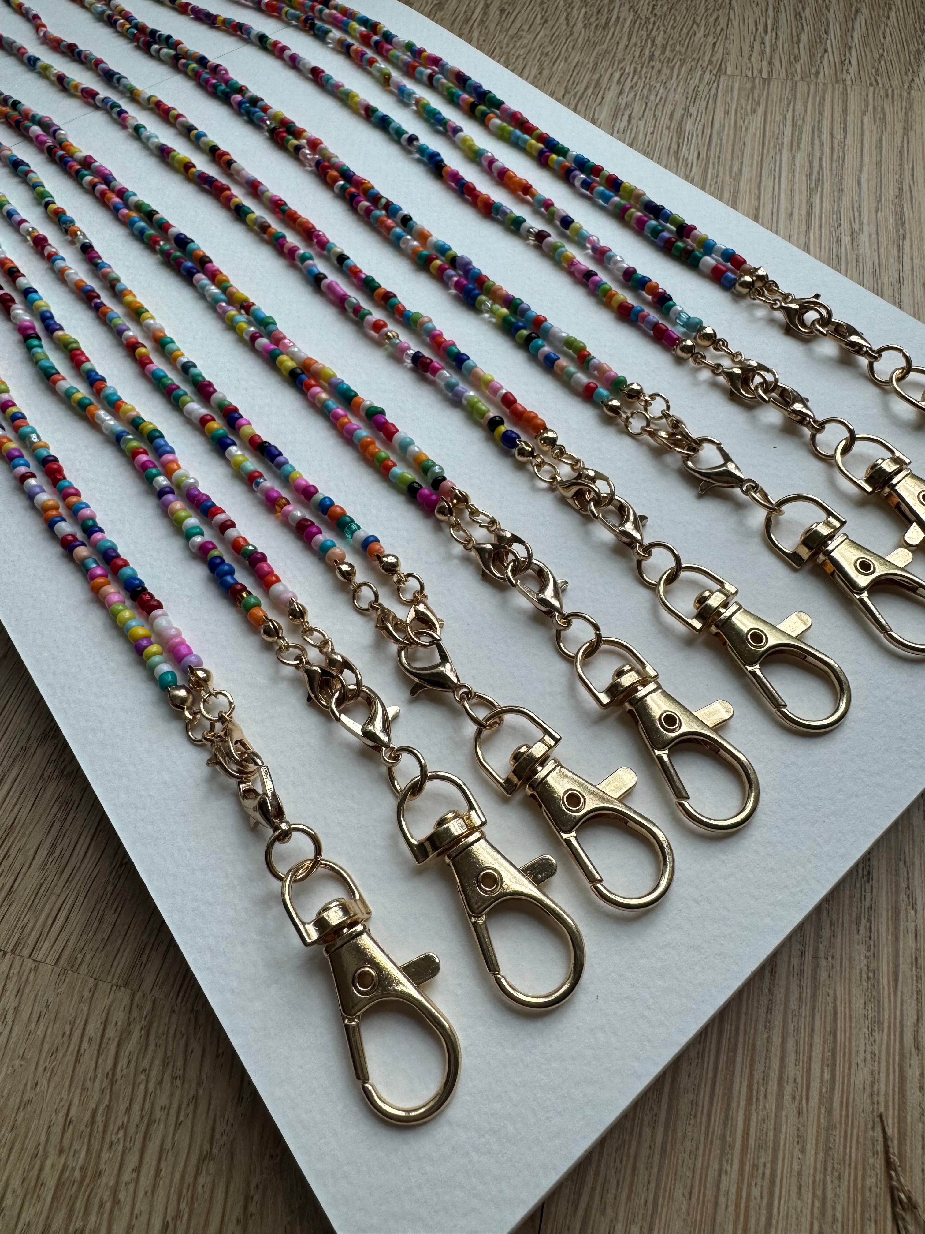 Picture of 8 multicolored beaded lanyards with gold clasps lined up next to each other.