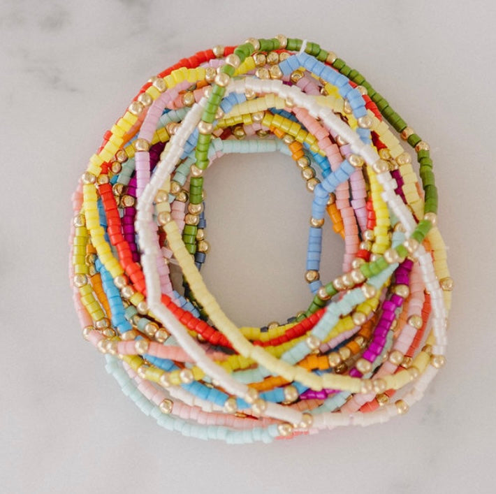 Picture of a stack of tiny beaded bracelets in greens, yellows, blues and pinks.