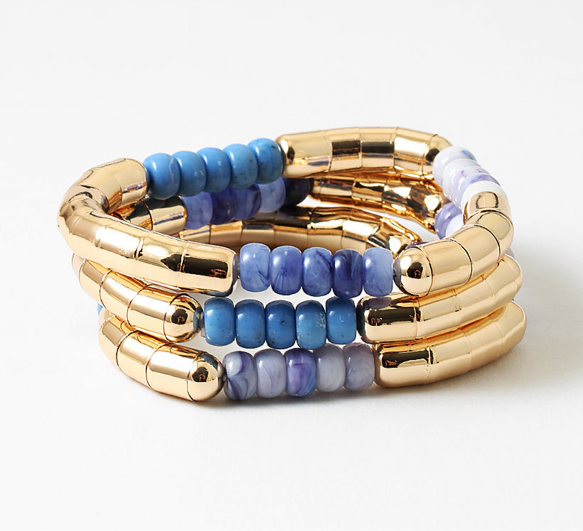 Stack of gold and blue beaded bracelets on a white background
