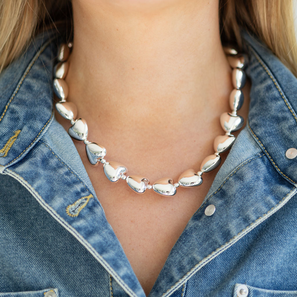Silver heart bead necklace worn by a person with a denim jacket