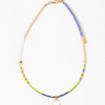 Dainty bead necklace in colors of blue, yellow, tan, green and white. Necklace has a small white disc pendant.