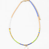 Dainty bead necklace in colors of blue, yellow, tan, green and white. Necklace has a small white disc pendant.
