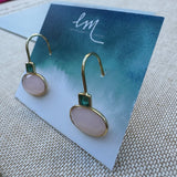 Gold dangle earrings with pink stones on a blue card with 'EM' branding.