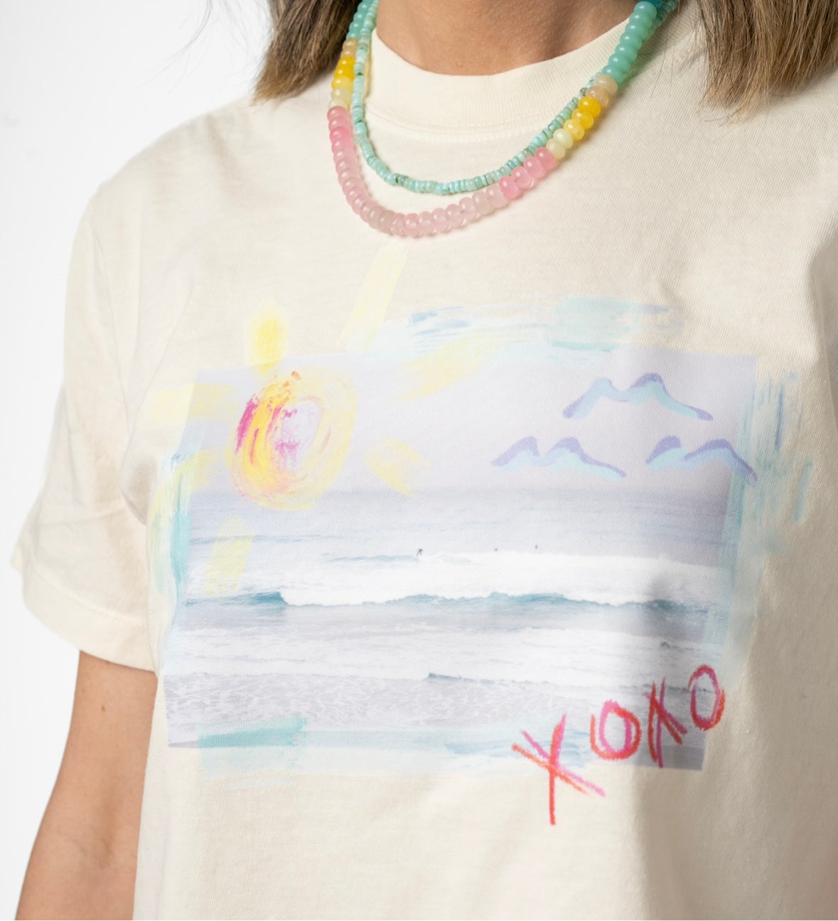 Person wearing a white t-shirt with a colorful abstract Beach design and 'XOXO' text.